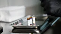 Primer plano de viales médicos y jeringa en bandeja de acero inoxidable en entorno clínico.