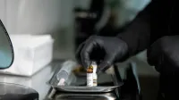 Close-up of gloved hands arranging medicine vials on a tray in a clinical setting.