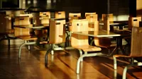 Sillas y mesas de madera vacías en un entorno de cafetería iluminado por el sol, proyectando sombras dramáticas.