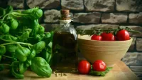 Imagen que muestra albahaca, tomates y un frasco de aceite de oliva.