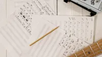 Vista de cerca de partituras, guitarra y lápiz, ideal para la creación e inspiración musical.