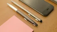 Stylish workspace featuring a smartphone, pens, and a notepad on a wooden desk.