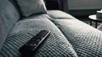 Un primer plano de un control remoto de TV en un sofá texturizado en un acogedor ambiente de sala de estar.