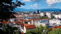 Impresionante vista aérea del paisaje urbano de Ljubljana con icónicos techos rojos, exuberante vegetación y montañas distantes.