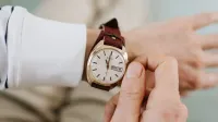 Un primer plano de una persona que ajusta un reloj de pulsera analógico con correa de cuero marrón vintage.
