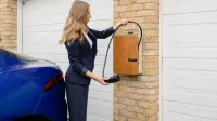 A woman using a home electric vehicle charger on a brick wall in a garage.