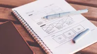 Close-up de un cuaderno con bocetos de estructura metálica y un smartphone en un escritorio de madera.