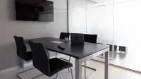 Sala de reuniones contemporánea con paredes de vidrio, computadora portátil y televisión para discusiones de negocios.