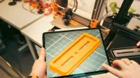 Una persona usa una tableta para ver un prototipo de modelo 3D en un taller equipado con impresoras 3D.