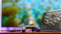 A modern gaming setup featuring a controller, laptop, and vibrant TV screen in a cozy home environment.