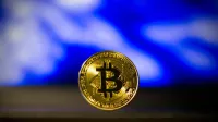 Close-up de una moneda de bitcoin de oro con un fondo abstracto azul borroso, simboliza la moneda digital.