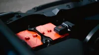 Detailed view of an orange car battery inside a vehicle's engine bay, highlighting its features.