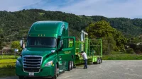 Un camión verde vívido con un remolque estacionado en un paisaje escénico con colinas y vegetación.