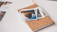 Cuaderno cubierto de corcho con fotografías impresas en un escritorio blanco, transmitiendo recuerdos de viaje.