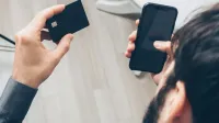 Close-up de hombre sosteniendo un teléfono inteligente y tarjeta de crédito, haciendo un pago en línea en interiores.
