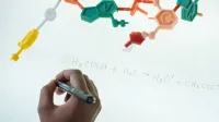 Escritura anónima de químico con marcador en tablero magnético iluminado Fórmula de producción de hidronio y acetato después de estudiar el modelo plástico de molécula en laboratorio