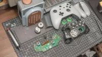 A disassembled video game controller and components set on a desk mat, illustrating electronics repair.