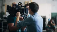 A film crew adjusting a video camera on an indoor set, focusing on technical preparation and teamwork.