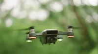 Un dron con luces rojas y verdes se cierne en un ambiente verde exuberante.