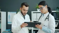 Dos médicos que revisan la información médica en una tableta en un entorno clínico.