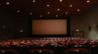 Un cine vacío con poca luz con filas de sillas rojas frente a una pantalla de proyector.