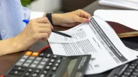 Primer plano de una persona que analiza documentos financieros usando una calculadora y un bolígrafo.