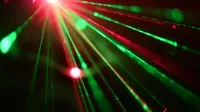Visualización dinámica de luces láser rojas y verdes que crean rayos vívidos a través de un fondo oscuro.