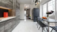 Table with fruits and flowers placed near window near counter and gray cupboards in stylish kitchen with fridge in apartment