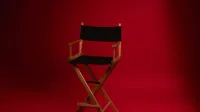 A wooden director's chair against a vibrant red backdrop, symbolizing film industry authority.