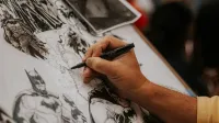 Artista dibujando personajes de cómic detallados con un bolígrafo en un evento animado.