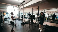 Detrás de escena de un documental de fitness siendo filmado en un gimnasio con equipo de iluminación profesional.