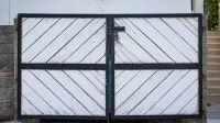 Una puerta de madera blanca rústica con paneles diagonales y un marco de metal negro en una entrada residencial.
