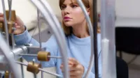 Una mujer con un suéter azul realiza un experimento de física en un laboratorio de ciencias. enfocado e intrigante.