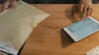 Persona que maneja la logística en una tableta con un paquete en una mesa de madera.
