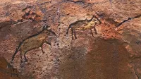 Vista detallada de tallas de roca prehistóricas que representan animales sobre una superficie escarpada.
