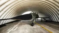 Un avión de combate estacionado dentro de un hangar militar arqueado, mostrando su elegante diseño.