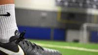 Una toma detallada de un taco de fútbol en un campo de césped interior, enfatizando el calzado y la actividad atlética.