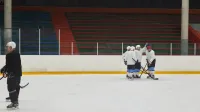 Group of athletes practicing ice hockey on an indoor rink with sticks and helmets.