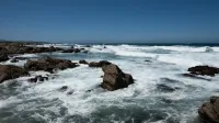 Impresionante costa de California con olas rompientes y rocas escarpadas bajo cielos azules despejados.