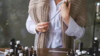 Configuración de aromaterapia con una mujer probando aceites esenciales usando tiras de aroma en una mesa de madera.