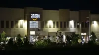 Edificio de almacén de Amazon iluminado por la noche con árboles y señalización.