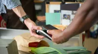 Un cliente que realiza un pago sin contacto con un teléfono inteligente en un mostrador de pago de una tienda de comestibles.