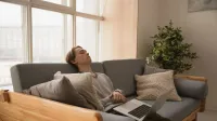 Person relaxing on a sofa indoors with a laptop, enjoying a peaceful moment.