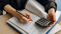 Un contador usando una calculadora y firmando papeleo, mostrando análisis financiero.