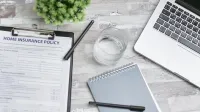 Lay flat de un espacio de trabajo con una póliza de seguro de hogar, una computadora portátil y un cuaderno en un escritorio.