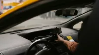 Conductor étnico masculino anónimo con volante usando el navegador GPS para buscar la dirección de conducción en la calle en la ciudad durante el trabajo