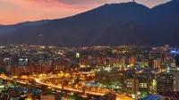 Una impresionante vista aérea del paisaje urbano de Caracas al anochecer, mostrando las vibrantes luces de la ciudad contra el telón de fondo montañoso.