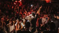 Concierto de rap vibrante con una multitud animada y un dinámico escenario en un bullicioso ambiente de discoteca.