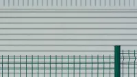 Valla de metal verde contrasta con una pared ondulada blanca, creando un patrón minimalista.