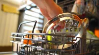 Person loading a dishwasher with kitchen utensils in a vibrant home setting.
